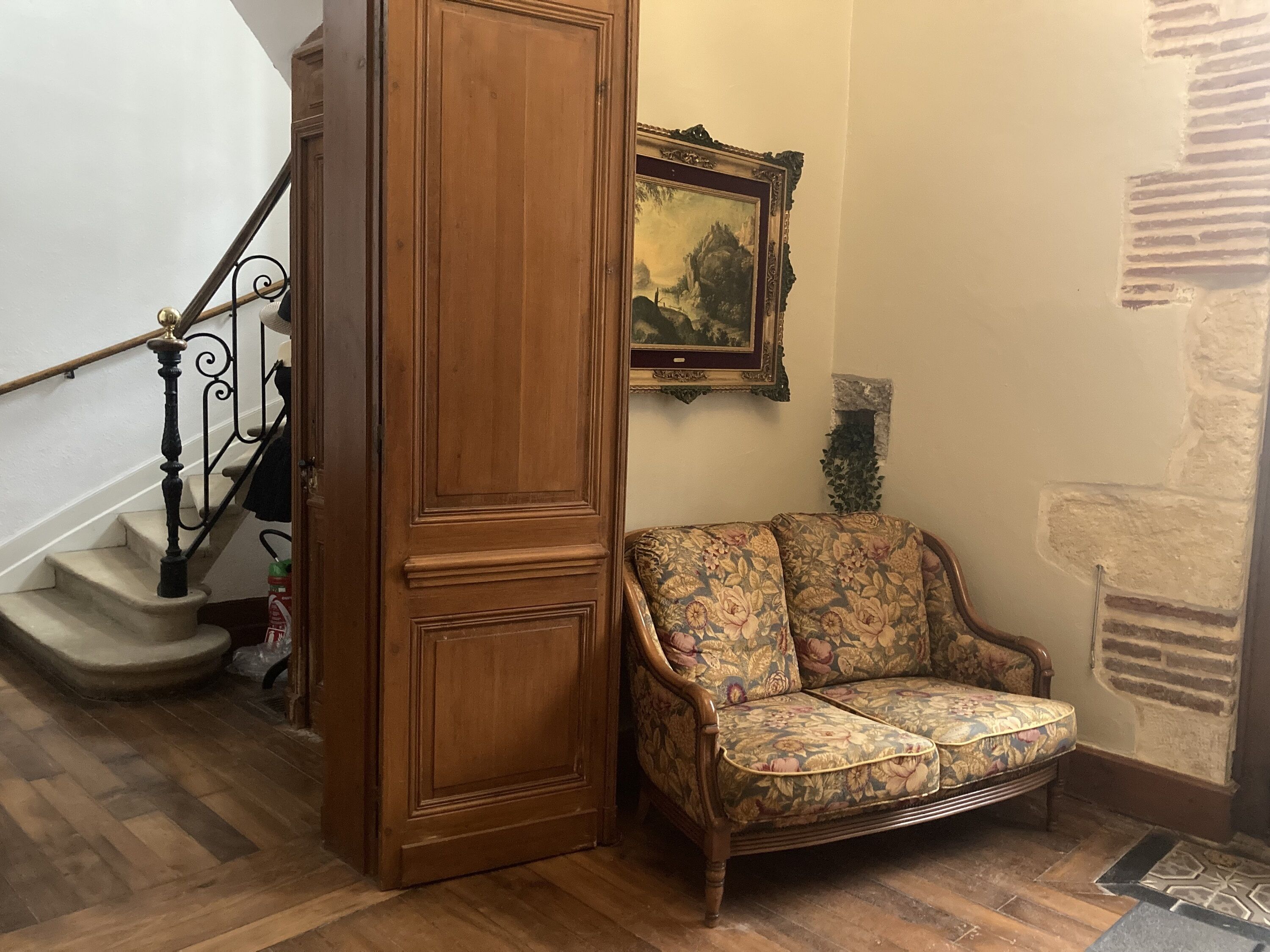 A staircase with a wooden handrail and a floral-patterned sofa in a corner.