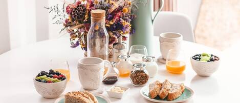 A breakfast setting with a table set for two, including a pitcher, cups, bowls of fruit, and bread.