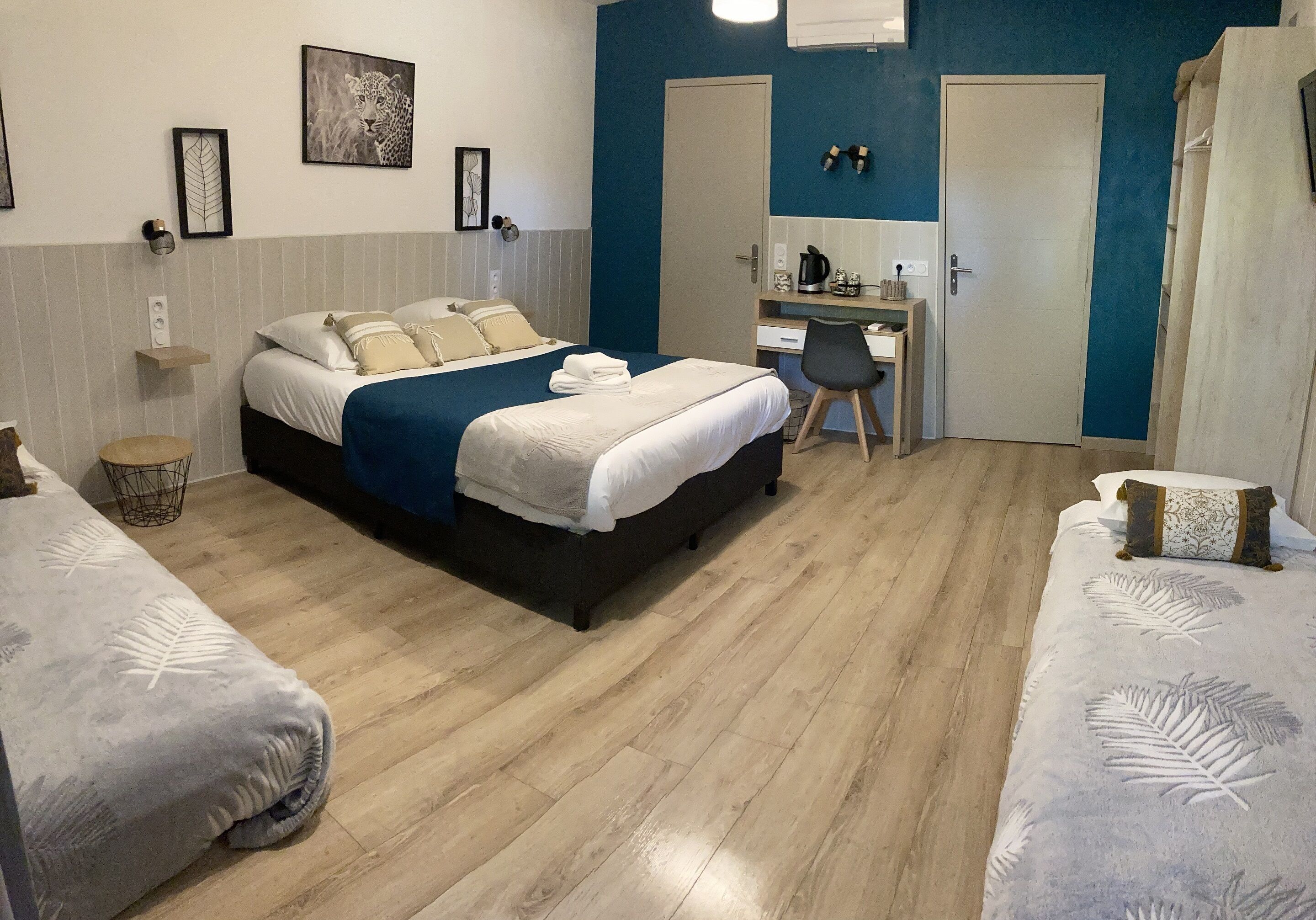 Une chambre d’hôtel avec un lit, un bureau et une chaise. Il y a deux portes, l’une avec un miroir et l’autre avec un interrupteur.
