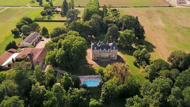 Vista aérea de una extensa propiedad con un edificio central rodeado de exuberante vegetación y una piscina.