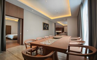 A hotel room with a long dining table, multiple chairs, a bed, and a painting on the wall.