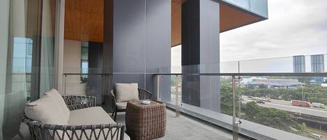 A balcony with wicker furniture, a glass railing, and a view of the cityscape.