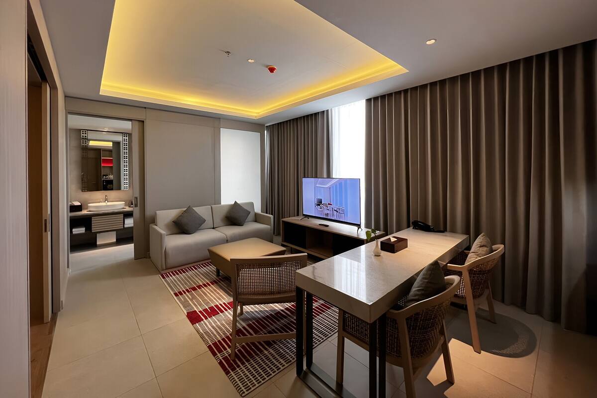 Una habitación de hotel moderna con una sala de estar que incluye un sofá, una mesa de comedor y un televisor.