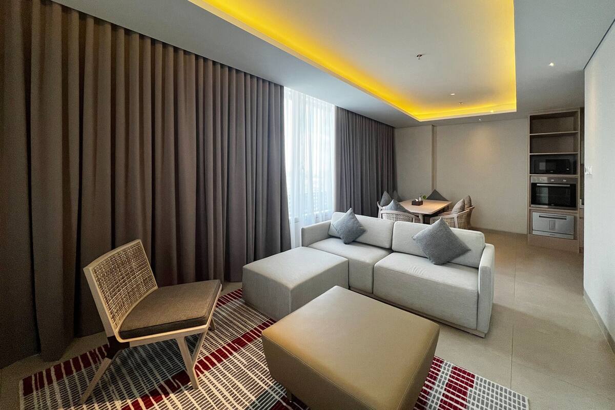 Una habitación de hotel moderna con sofá, reposapiés, sillón, mesa de comedor y horno empotrado.