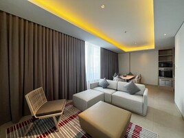 A modern hotel room with a sofa, ottoman, chair, dining table, and built-in oven.