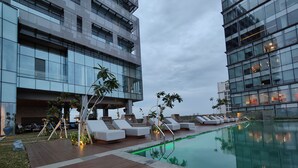 A rooftop pool area with lounge chairs and a modern building in the background. - Ra Suites Simatupang (Jakarta)