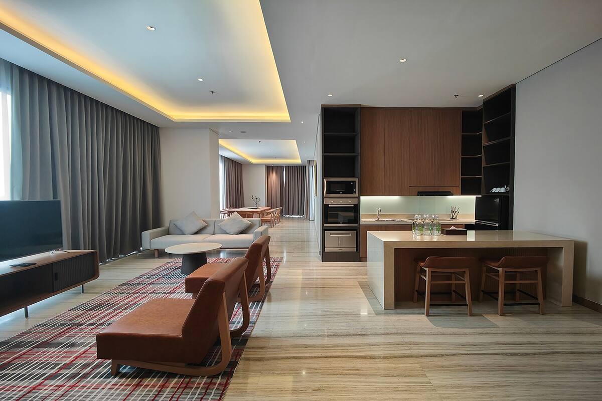 Una habitación de hotel moderna con sofá, televisión y zona de comedor con sillas y una mesa.