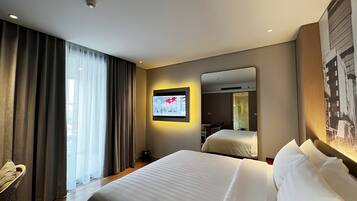Habitación de hotel con una cama grande, un televisor montado en la pared y una ventana con cortinas.