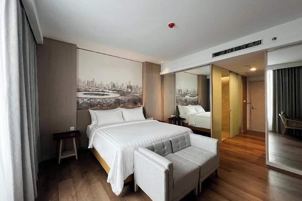 Habitación de hotel moderna con una cama grande, un área de descanso, un mural con un paisaje urbano y una puerta corrediza a un balcón.