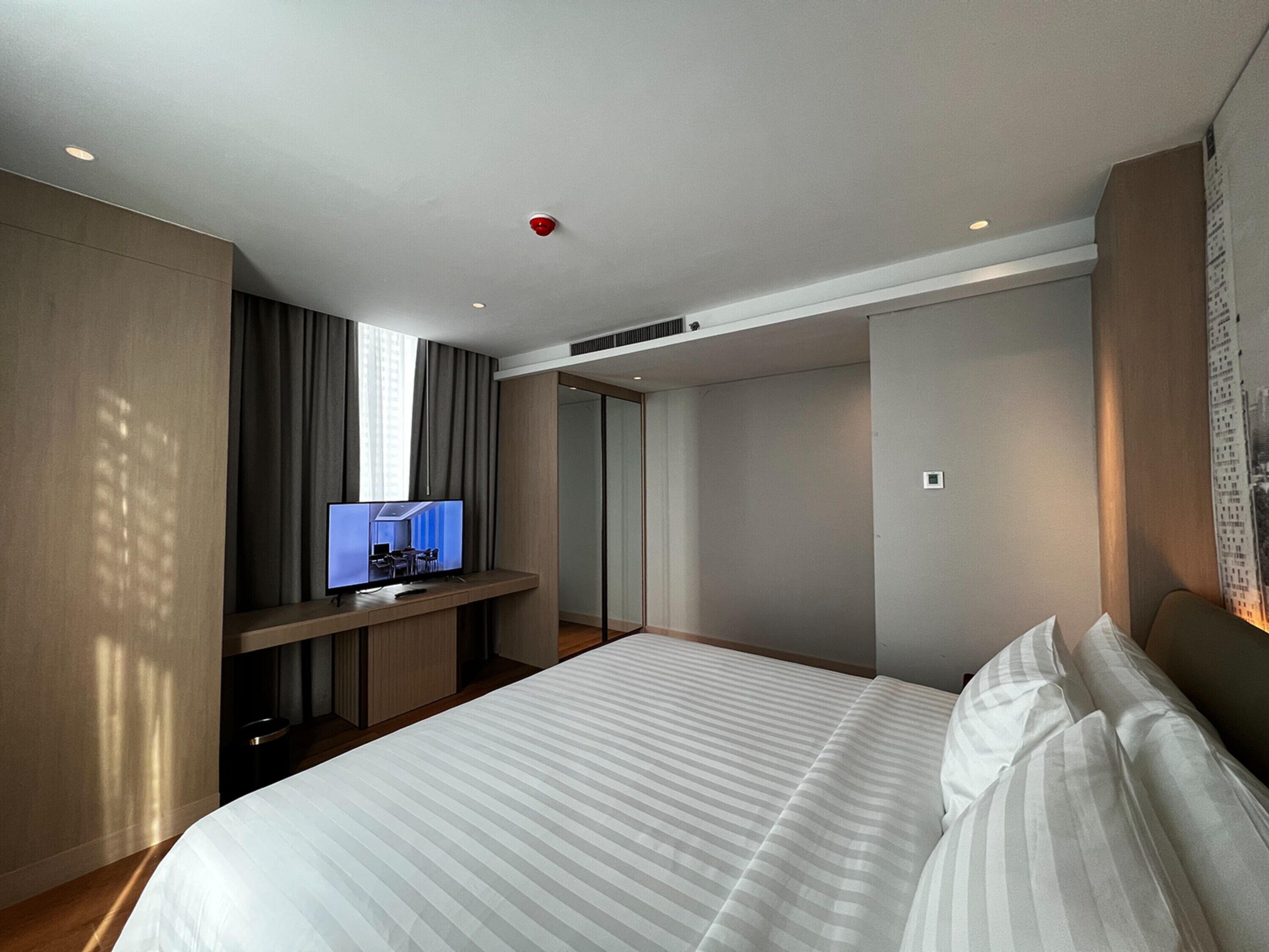 A modern hotel room with a large bed, a flat-screen TV on a wooden console, and a cityscape view through the window.
