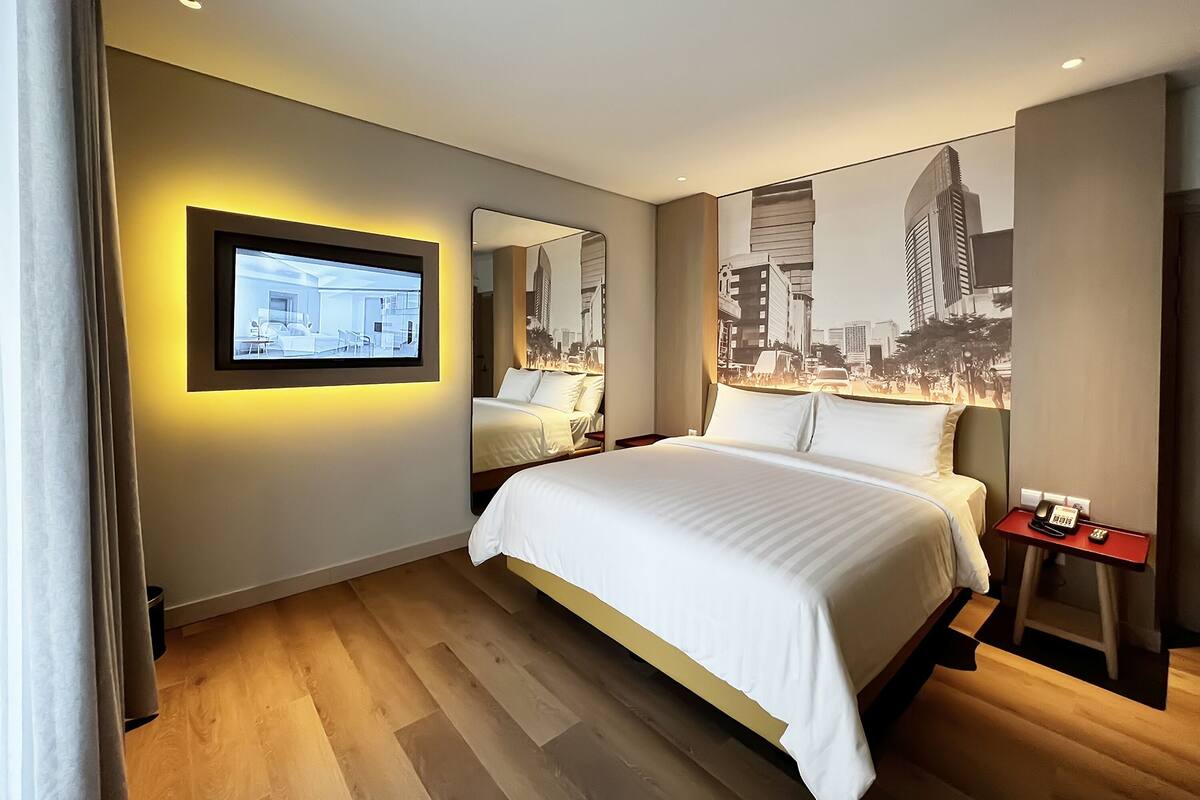 Habitación de hotel moderna con una cama grande, un mural con vista a la ciudad, un televisor de pantalla plana y una mesita de noche con teléfono.