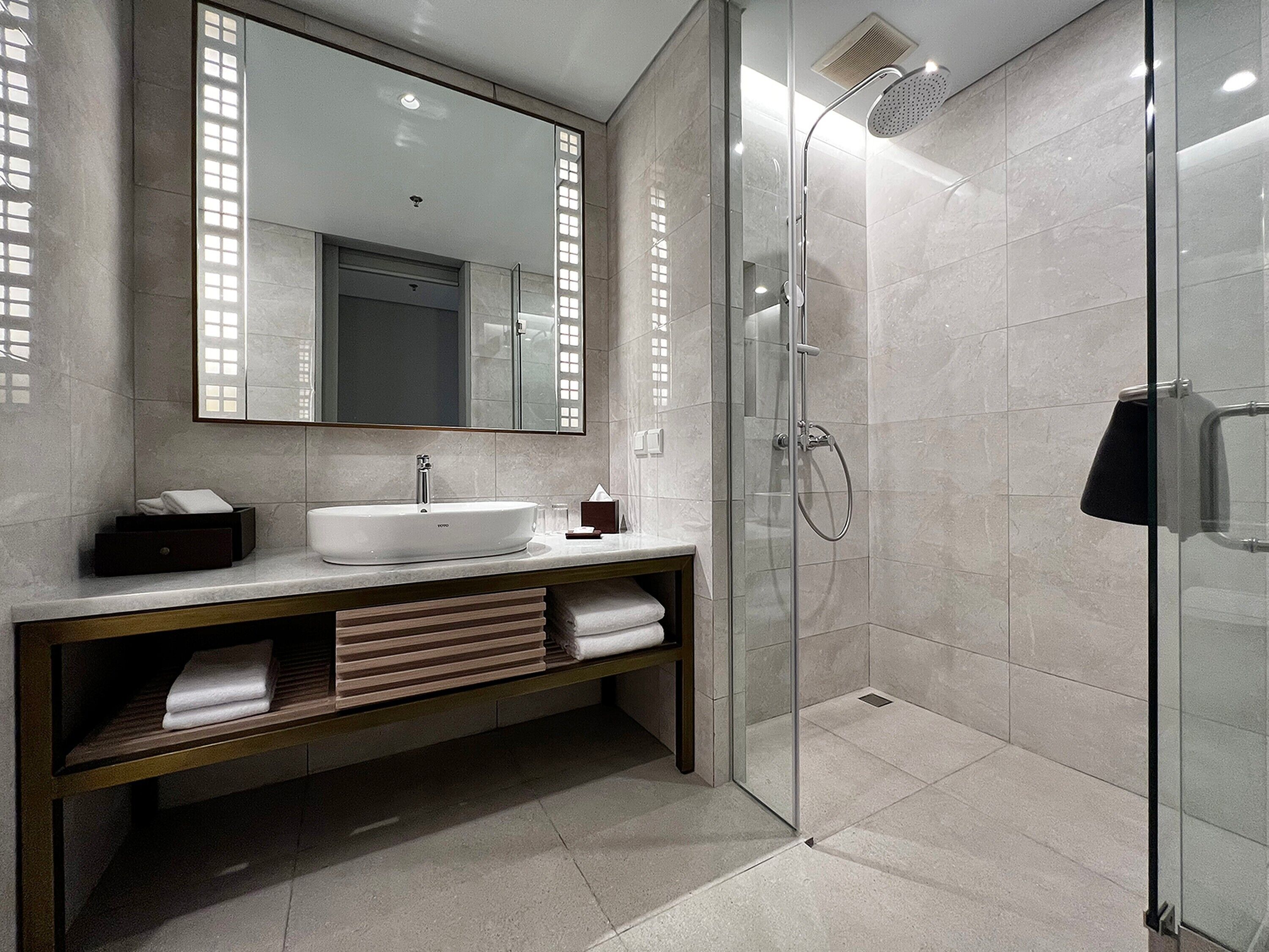 Une salle de bain moderne dotée d’une douche à parois de verre, d’un grand miroir et d’un meuble-lavabo avec un espace pour ranger les serviettes.