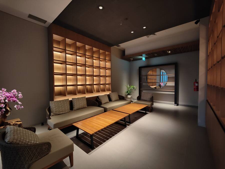 Un área de estar moderna con un conjunto de sofás, una mesa de centro de madera y una unidad de estanterías fijada a la pared con iluminación empotrada.
