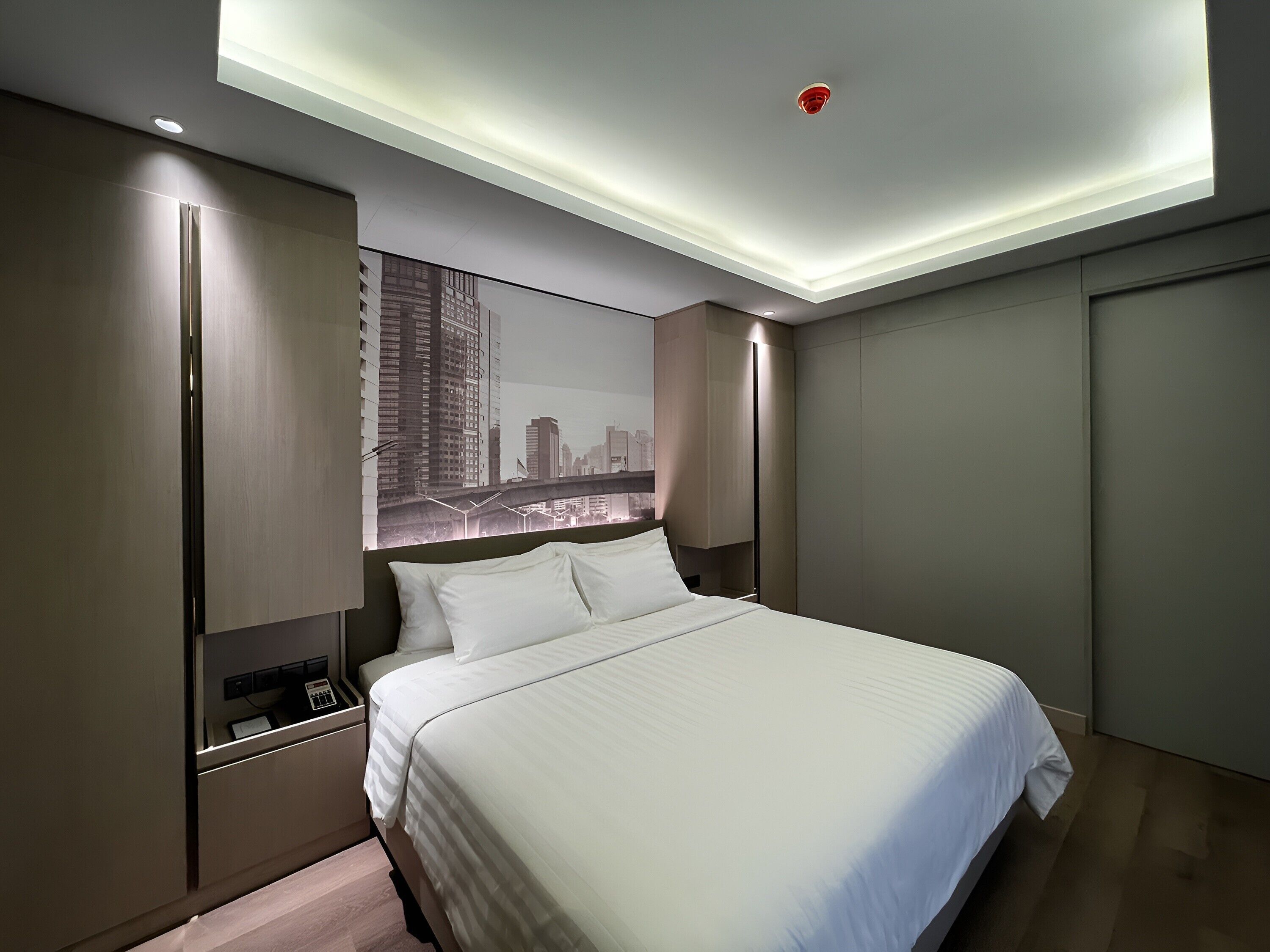 Habitación de hotel moderna con una cama grande, vistas a la ciudad, armario empotrado y mesita de noche con teléfono.