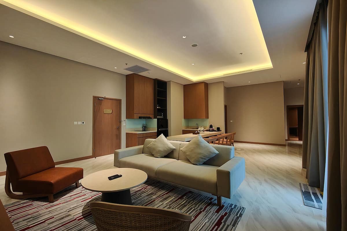 Una sala de estar moderna con sofá, sillón y mesa de centro, comunicada con una cocina que tiene armarios de madera.