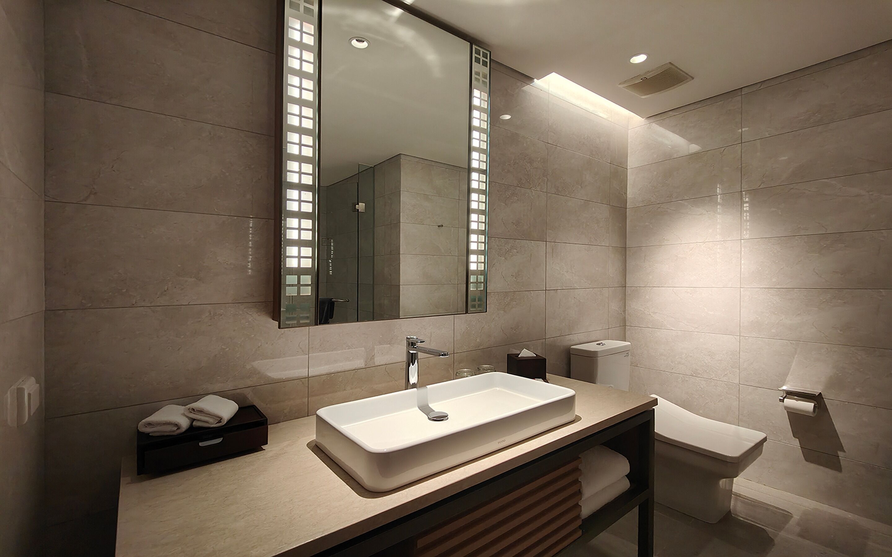 A modern bathroom with a large mirror, a rectangular sink, a toilet, and a towel rack.