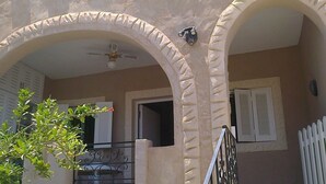 A building with two arched doorways, a ceiling fan, and a white picket fence.