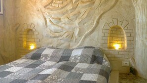 A bedroom with a checkered bedspread, two wall-mounted lights, and a textured wall resembling a tree trunk.