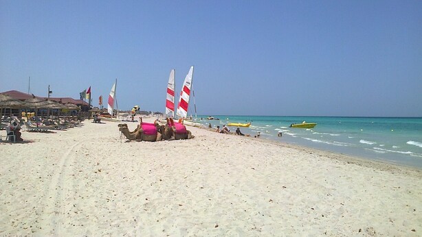 A beach with a sandy shore, a few people, and a few boats.