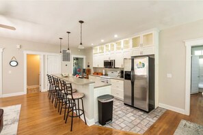 A modern kitchen with a central island, bar stools, a stainless steel refrigerator, and white cabinetry.
