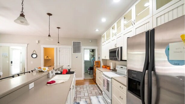 A modern kitchen with a large island, stainless steel appliances, and white cabinetry. - The Queen B (Oak Island)