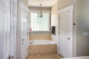 A bathroom with a freestanding bathtub, a window with a view, and a chandelier.