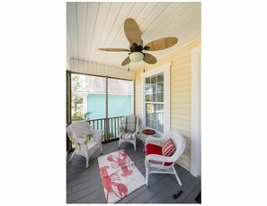 A covered porch with wicker furniture, a ceiling fan, and a view of a house.