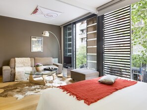 Quarto moderno com cama grande, mesa de centro de vidro, sofá e televisão.