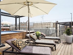 Terraço no telhado com piscina, espreguiçadeiras e um grande guarda-sol.