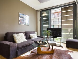Uma sala de estar moderna com um sofá, uma mesa de centro de vidro e uma janela grande com persianas.