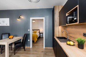 Une cuisine moderne équipée d’un four à micro-ondes encastré, d’un évier et d’un plan de travail orné de citrons. On y trouve également un coin repas avec une table et des chaises, et une chambre à coucher visible à travers une porte ouverte.