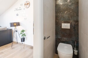 A modern bathroom with a white toilet, a wall-mounted light switch, and a decorative world map clock.