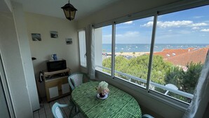 A balcony with a table and chairs, a TV, and a view of the sea and buildings. - Beautiful 1-bedroom apartment near the beach, with parking and garage (Arcachon)