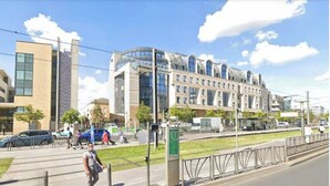 Ein modernes Gebäude mit Glas- und Backsteinfassaden, einem Fußweg und einer Straße mit Autos.