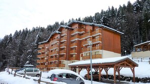Um hotel com várias andares, varandas de madeira e paisagem de estação de esqui ao fundo.
