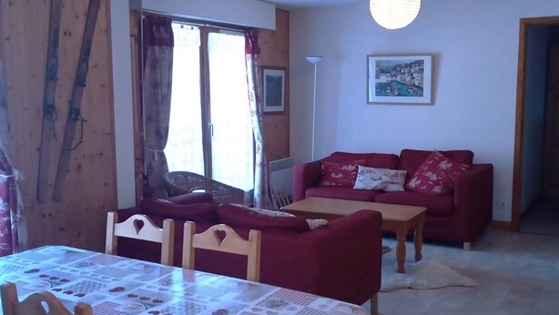 Uma sala de estar acolhedora com um sofá vermelho, uma mesa de jantar de madeira e uma grande janela com cortinas.