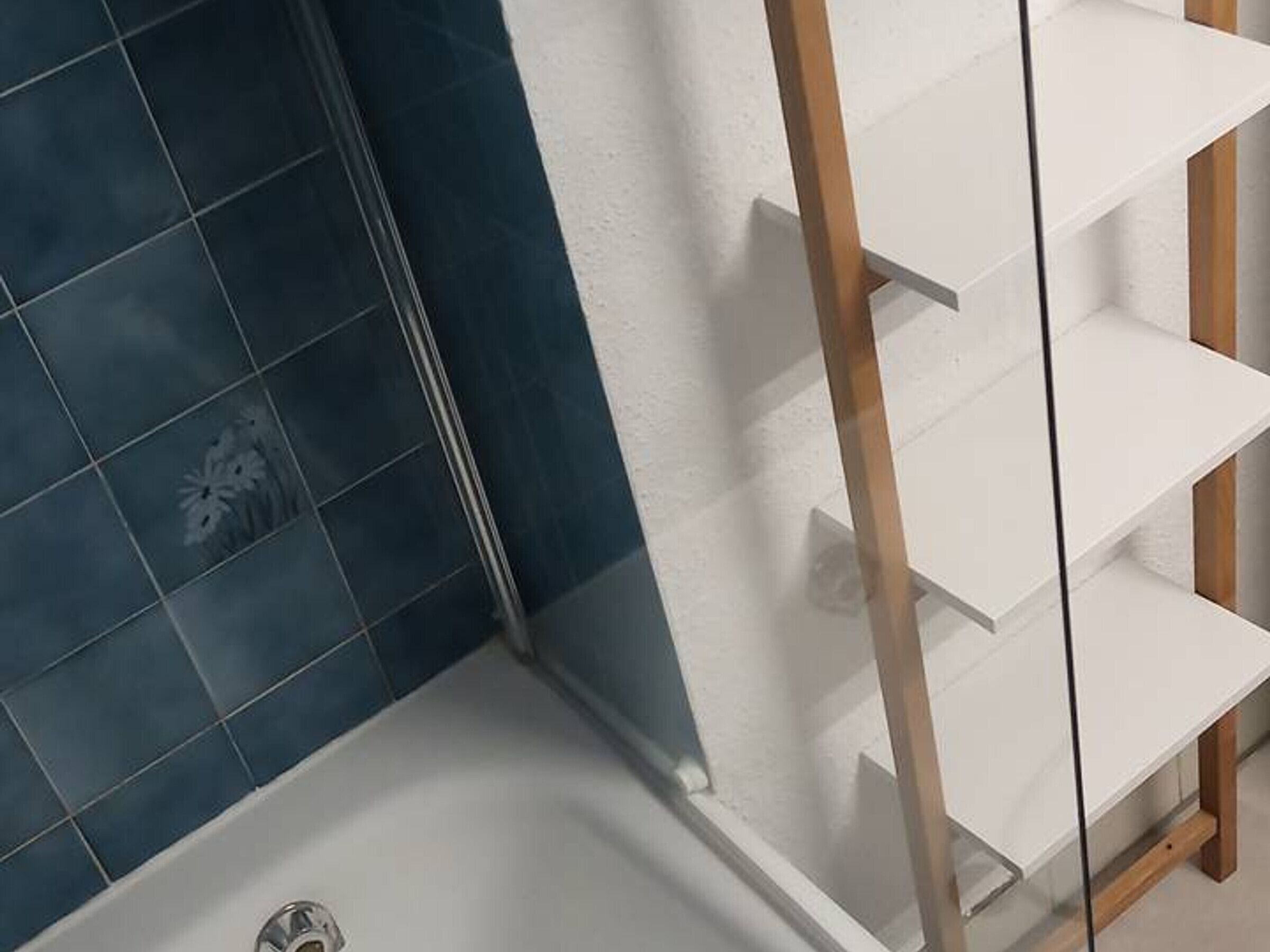 A bathroom with dark blue tiles, a white bathtub, and a wooden shelf unit.