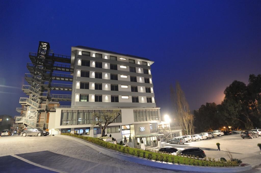 A modern hotel with a multi-story structure, a parking lot, and a staircase leading to the entrance.