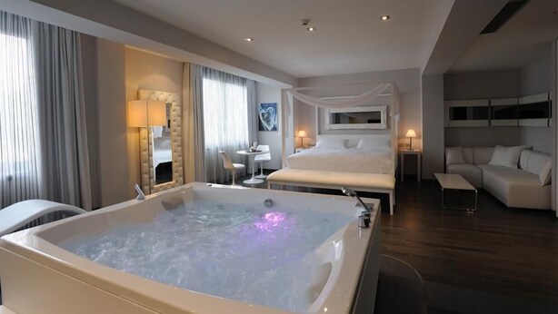 A modern hotel room with a large bathtub, a bed, a sofa, and a desk with a chair. - Park Hotel Sporting (Teramo)