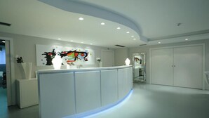 A modern reception area with a curved reception desk, a large abstract painting on the wall, and a large mirror reflecting the room. - Park Hotel Sporting (Teramo)