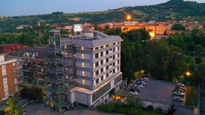 A multi-story hotel with a modern design, featuring a prominent staircase, a parking lot, and a view of surrounding buildings and hills. - Park Hotel Sporting (Teramo)