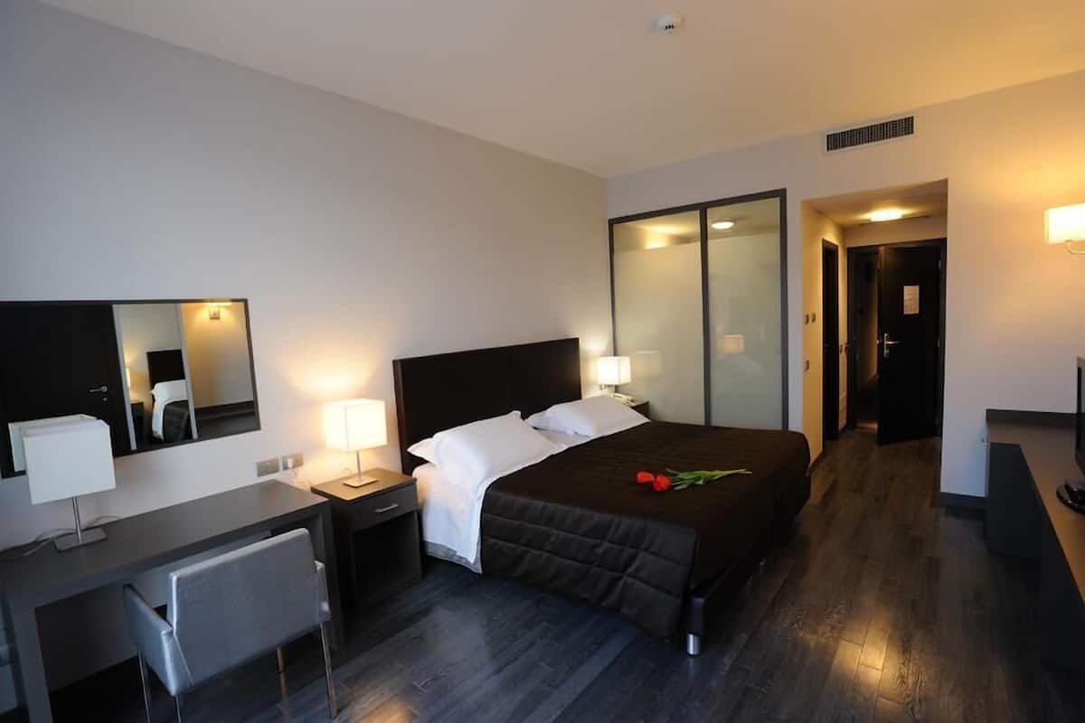A modern hotel room with a bed, bedside tables, a desk, and a chair.