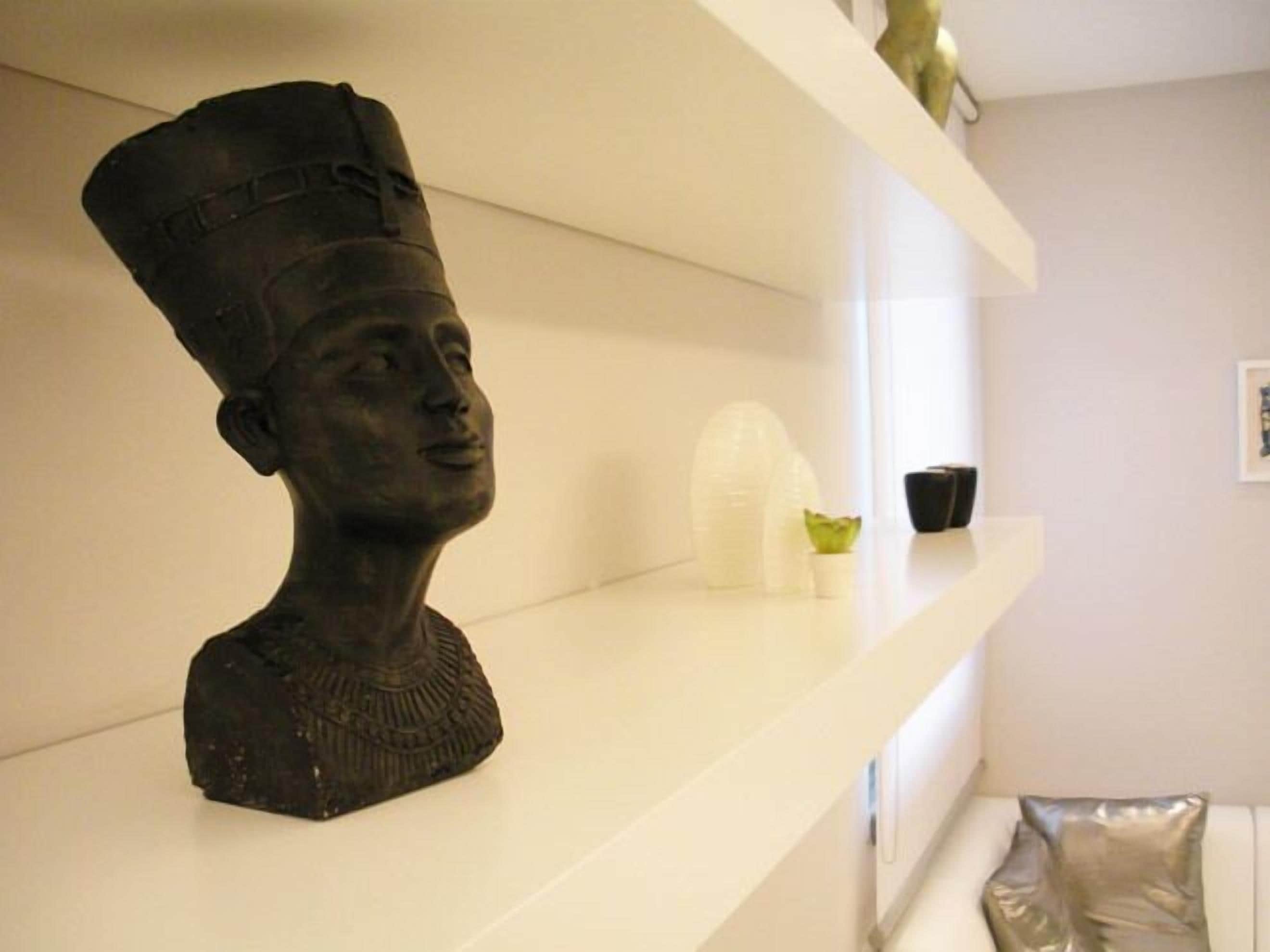 A bust sculpture on a white shelf in a room with a white couch and a framed picture on the wall.