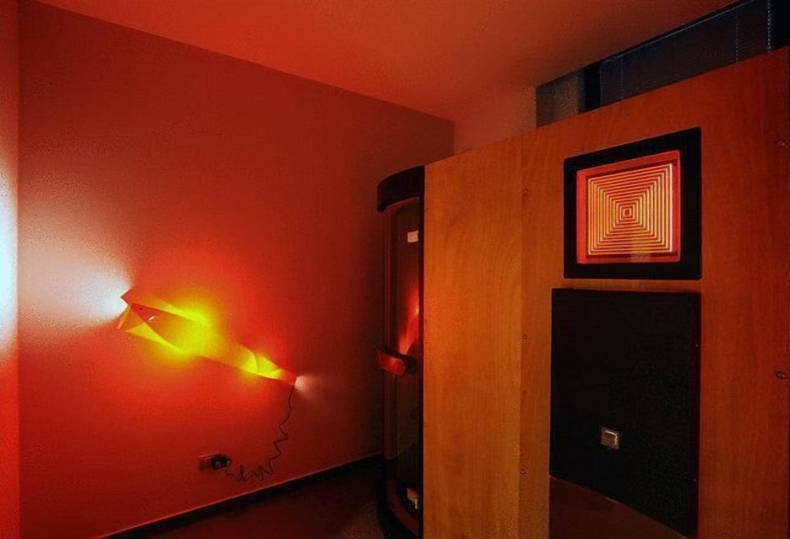 Una habitación con una puerta de madera, un aplique en la pared y una pequeña rejilla cuadrada.