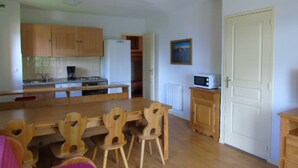 A compact kitchen with wooden cabinets, a built-in stove, and a microwave. There is a dining table with chairs and a white door in the background. - Apartment for 8 with balcony near cable car and shops (Valfréjus)