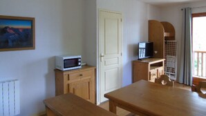 A room with a wooden table, a microwave on a small cabinet, a door, and a window with curtains. - Apartment for 8 with balcony near cable car and shops (Valfréjus)