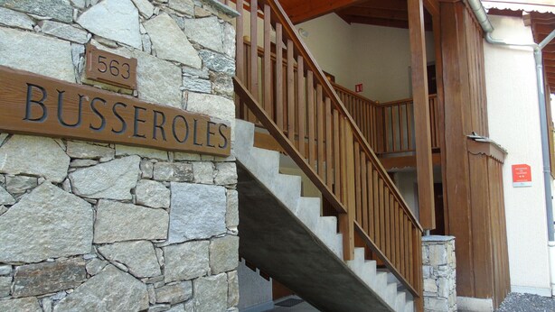 A stone wall with a wooden sign reading "BUSSEROLLES" and a wooden staircase leading to a wooden door. - Apartment for 8 with balcony near cable car and shops (Valfréjus)