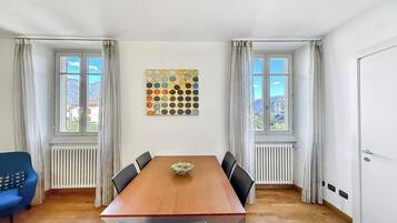 Ett matrum med ett träbord, sex stolar, en dekorativ väggdekoration och två fönster med gardiner.
