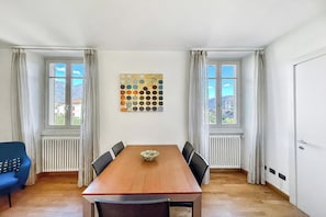 Een eetkamer met een houten tafel, zes stoelen, een decoratief wandobject en twee ramen met gordijnen.