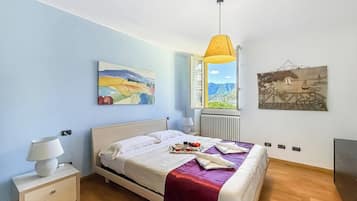 Un dormitorio con cama, mesita de noche, lámpara, ventana con vistas y dos obras de arte colgadas en la pared.